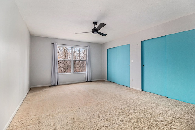 unfurnished bedroom featuring baseboards, ceiling fan, a textured ceiling, carpet floors, and two closets