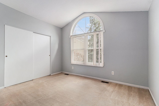 unfurnished bedroom with carpet, a closet, visible vents, vaulted ceiling, and baseboards