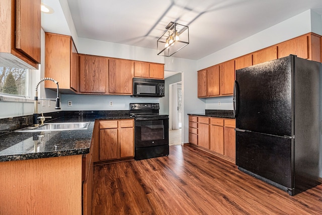 kitchen with dark wood-type flooring, brown cabinetry, a sink, dark stone counters, and black appliances