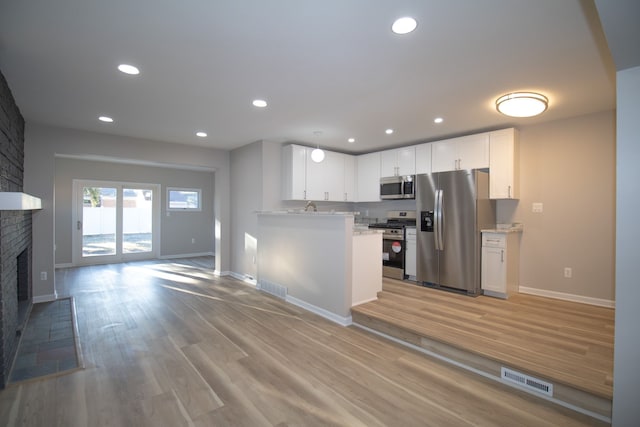 kitchen featuring stainless steel appliances, visible vents, light wood-style floors, a brick fireplace, and open floor plan