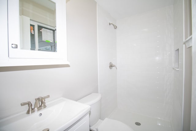 full bath with vanity, a tile shower, and toilet