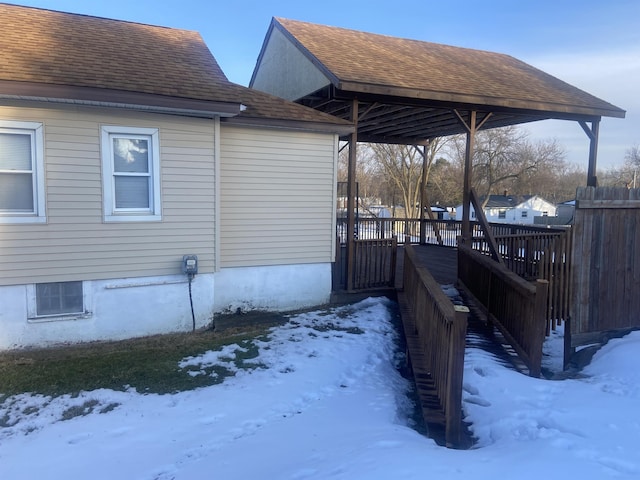 view of snowy exterior with roof with shingles and fence