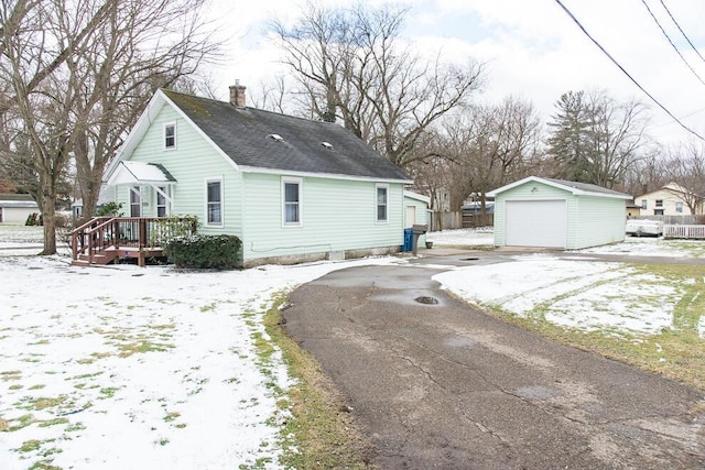 snow covered property with a chimney, a shingled roof, a garage, an outdoor structure, and driveway