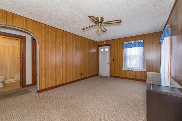 empty room featuring carpet, wood walls, arched walkways, and a textured ceiling