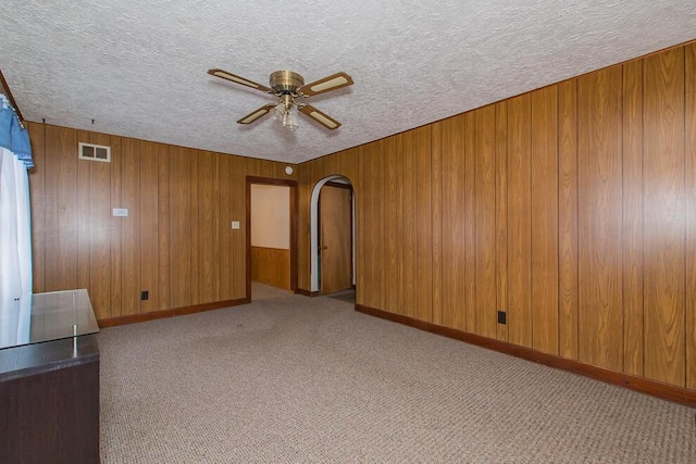 spare room with a textured ceiling, ceiling fan, arched walkways, visible vents, and carpet