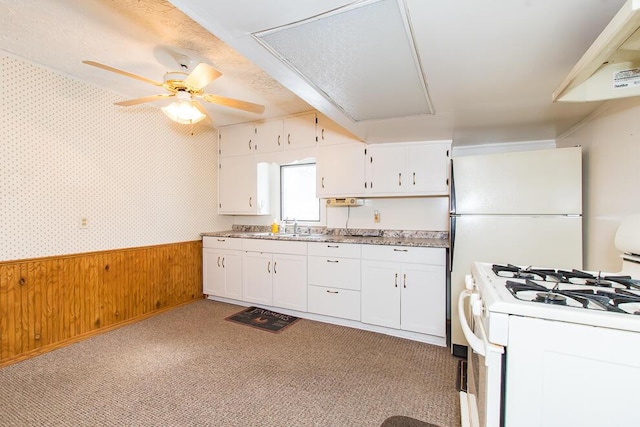 kitchen with a wainscoted wall, white cabinets, a sink, white appliances, and wallpapered walls