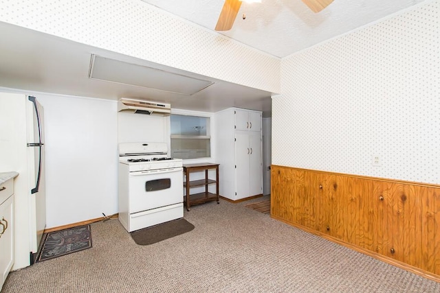 kitchen with white appliances, wallpapered walls, a ceiling fan, a wainscoted wall, and under cabinet range hood