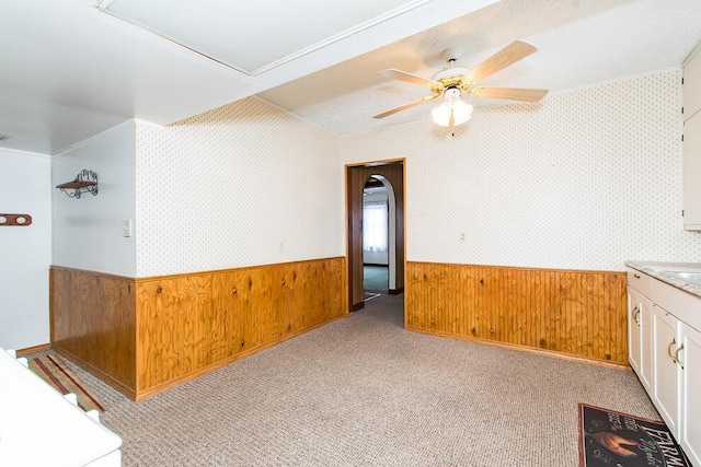 spare room with light colored carpet, a wainscoted wall, wood walls, a ceiling fan, and wallpapered walls