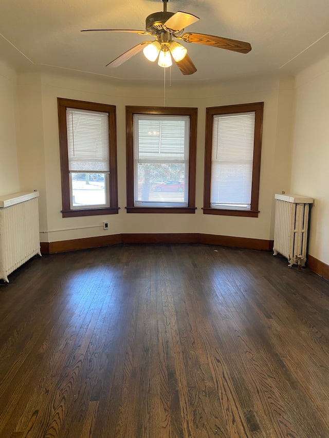 empty room with dark wood-style flooring, radiator, radiator heating unit, ceiling fan, and baseboards