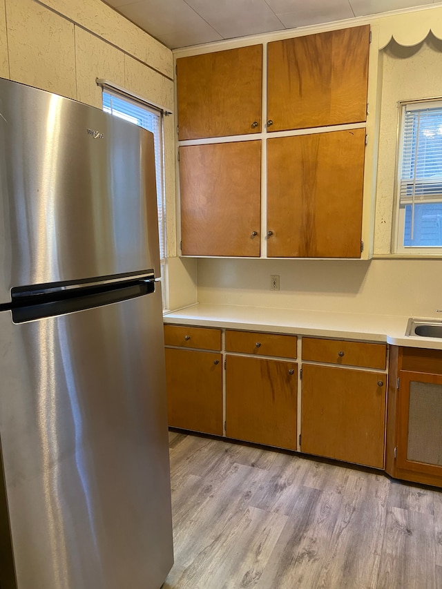 kitchen featuring brown cabinetry, light wood-style flooring, light countertops, and freestanding refrigerator