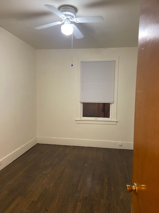 spare room featuring dark wood-type flooring, a ceiling fan, and baseboards