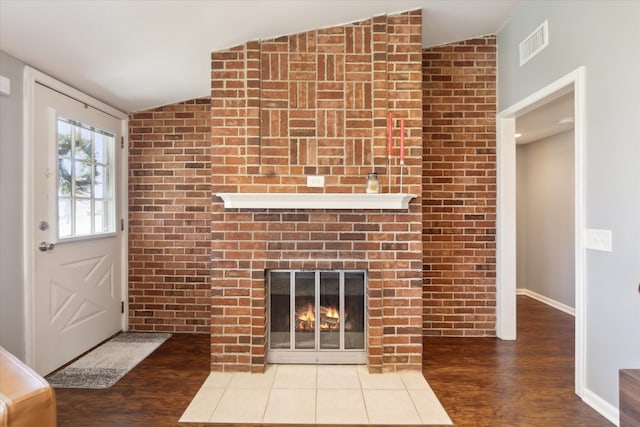 unfurnished living room with visible vents, wood finished floors, baseboards, a brick fireplace, and vaulted ceiling