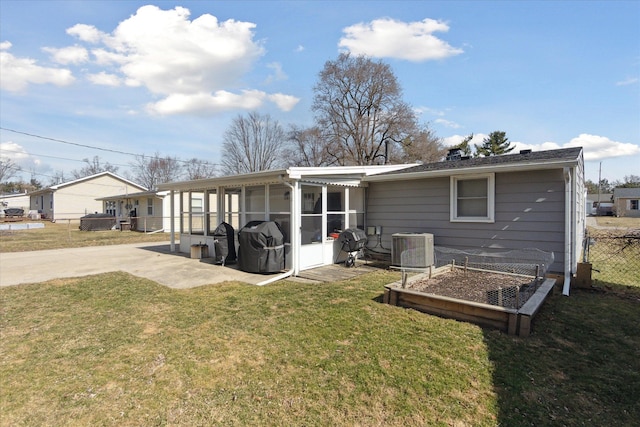 back of house featuring fence, central AC unit, a vegetable garden, a sunroom, and a lawn