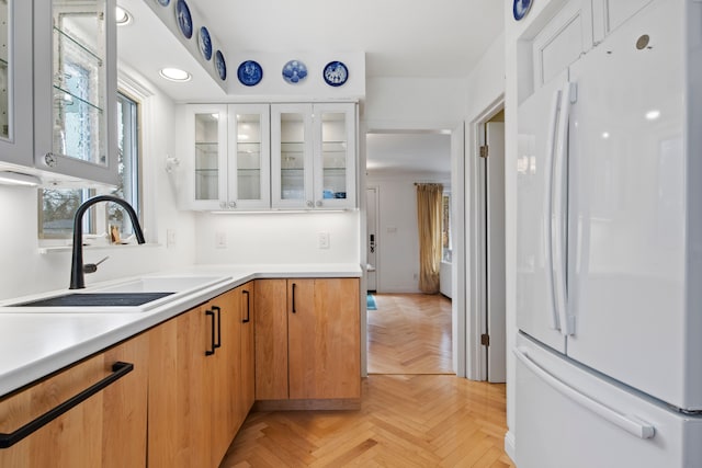 kitchen featuring glass insert cabinets, light countertops, freestanding refrigerator, white cabinetry, and a sink