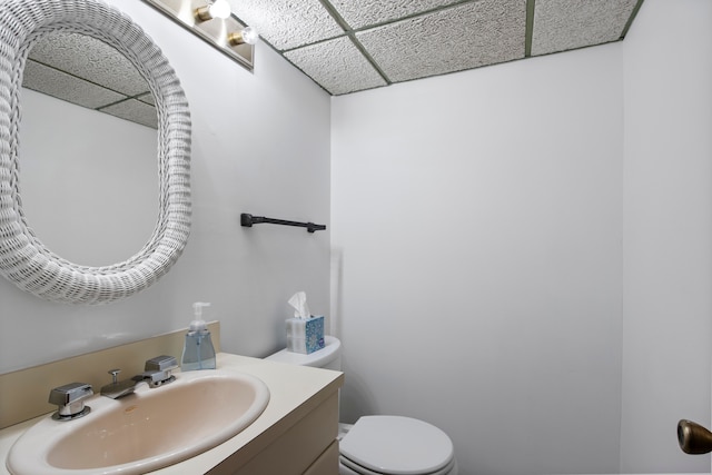 half bath with a drop ceiling, toilet, and vanity