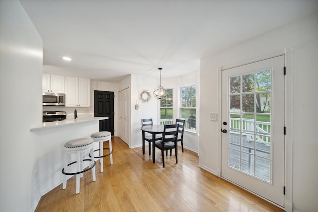 kitchen with white cabinets, appliances with stainless steel finishes, a breakfast bar, light countertops, and light wood-type flooring