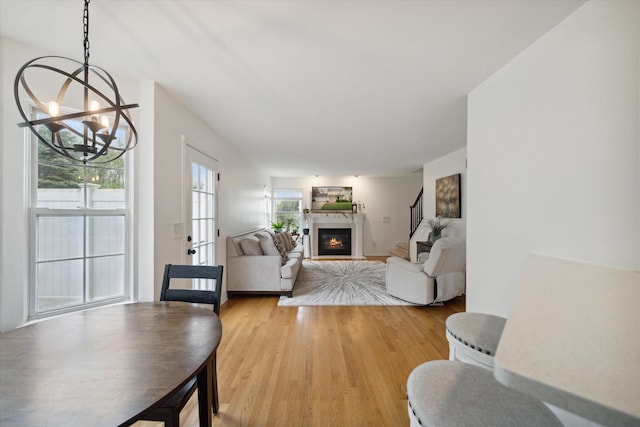 living area featuring light wood-style floors, stairway, a chandelier, and a glass covered fireplace