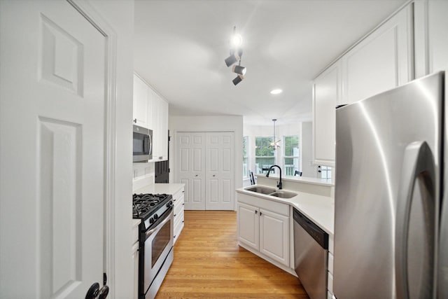 kitchen with white cabinets, light wood-style flooring, stainless steel appliances, and a sink