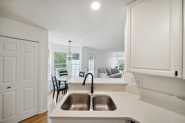 kitchen with a sink, light countertops, white cabinetry, pendant lighting, and a notable chandelier