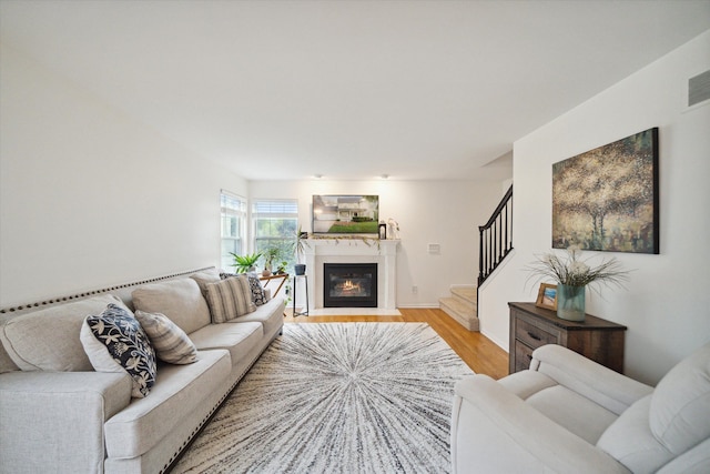 living area featuring baseboards, visible vents, a fireplace with flush hearth, stairway, and wood finished floors