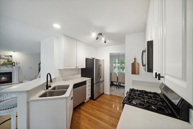 kitchen featuring stainless steel appliances, light countertops, a glass covered fireplace, white cabinetry, and a sink