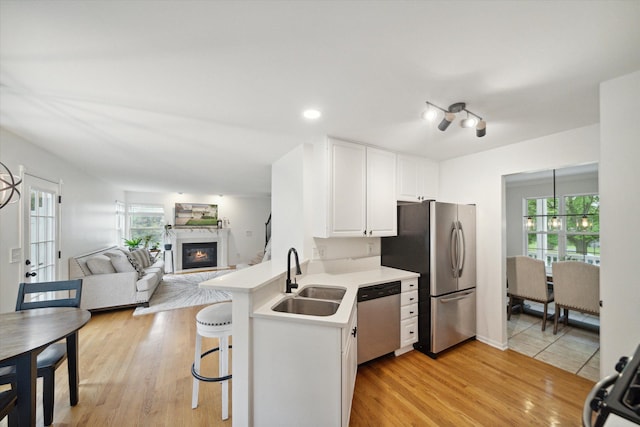 kitchen featuring stainless steel appliances, light countertops, a glass covered fireplace, white cabinets, and a sink