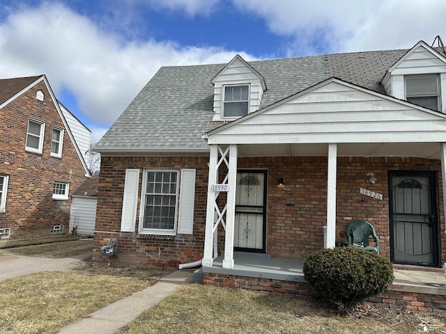 view of front of property with covered porch, brick siding, and roof with shingles