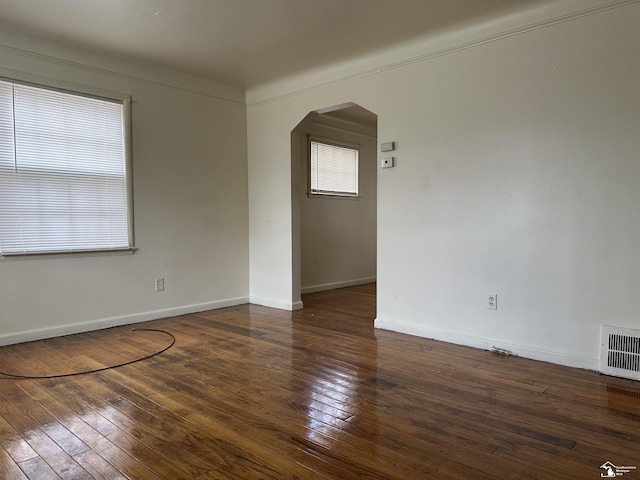 empty room with baseboards, visible vents, arched walkways, and hardwood / wood-style floors