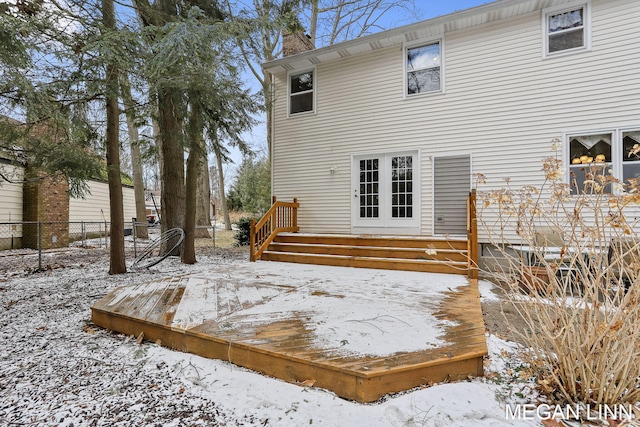 snow covered back of property featuring a chimney, a wooden deck, and fence