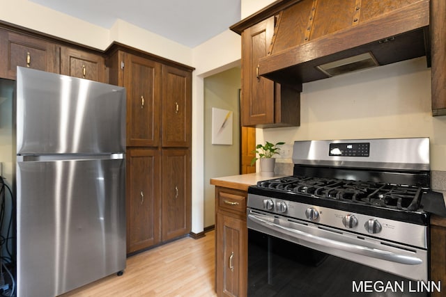 kitchen with under cabinet range hood, stainless steel appliances, light wood finished floors, and light countertops