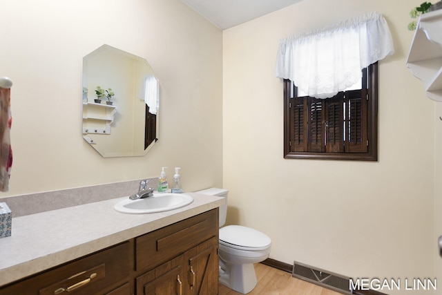 bathroom featuring visible vents, toilet, vanity, wood finished floors, and baseboards