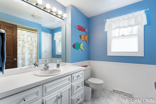 bathroom with a healthy amount of sunlight, a wainscoted wall, visible vents, and toilet