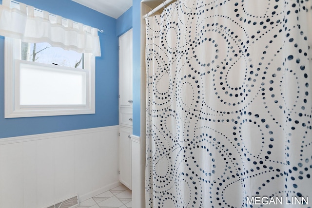 bathroom with curtained shower, tile patterned flooring, wainscoting, and visible vents