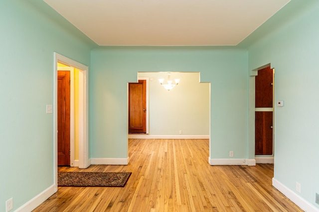 spare room with wood-type flooring, a chandelier, and baseboards