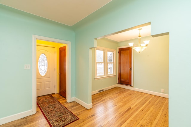 foyer featuring baseboards, light wood-type flooring, visible vents, and an inviting chandelier