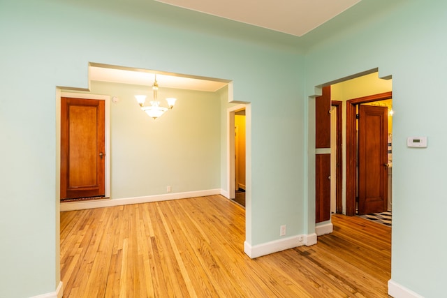 unfurnished room with light wood finished floors, baseboards, and a notable chandelier