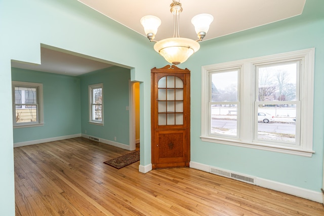 unfurnished dining area featuring a wealth of natural light, an inviting chandelier, visible vents, and light wood-style floors