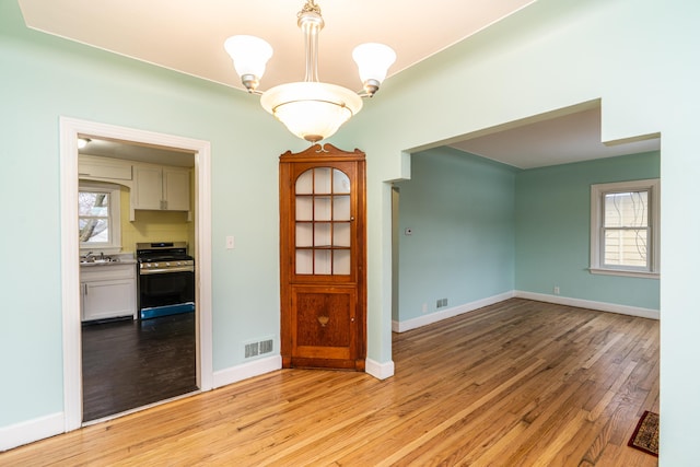 unfurnished room featuring light wood finished floors, a sink, a wealth of natural light, and baseboards