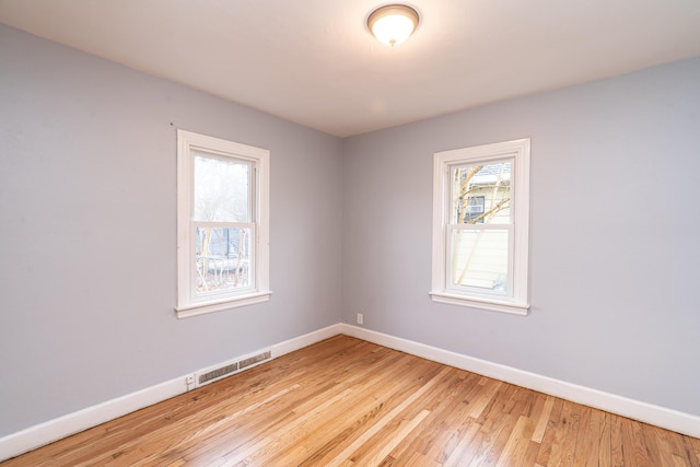 empty room featuring baseboards, light wood-style flooring, visible vents, and a healthy amount of sunlight