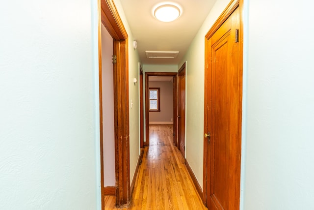 corridor featuring light wood-style floors, attic access, visible vents, and baseboards