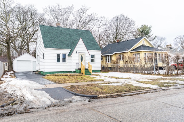 view of front facade with an outbuilding, a detached garage, a shingled roof, fence, and driveway