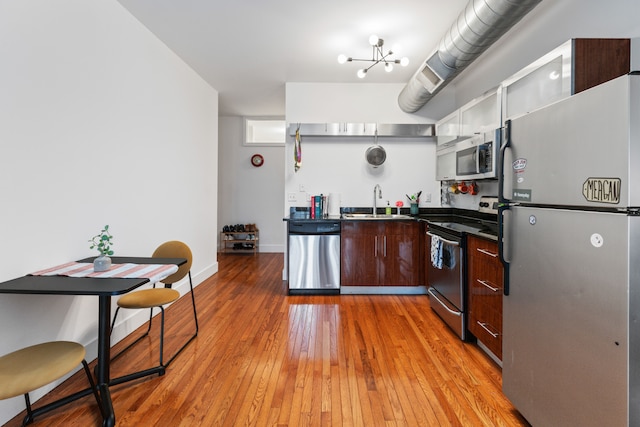 kitchen featuring baseboards, a sink, stainless steel appliances, dark countertops, and light wood-type flooring