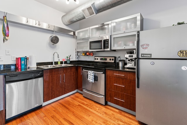 kitchen featuring a sink, glass insert cabinets, light wood-style floors, appliances with stainless steel finishes, and modern cabinets