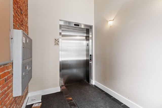 kitchen with mail area, dark tile patterned flooring, elevator, brick wall, and baseboards