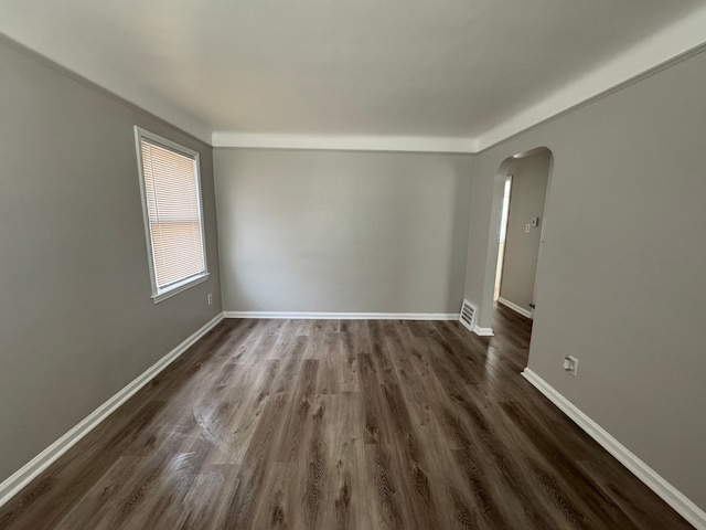 empty room with arched walkways, dark wood-style flooring, visible vents, and baseboards