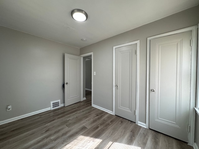 unfurnished bedroom with a closet, visible vents, baseboards, and wood finished floors