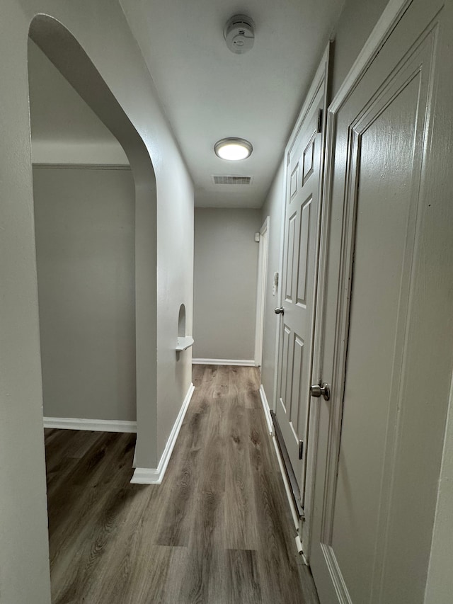 hall featuring arched walkways, dark wood finished floors, visible vents, and baseboards