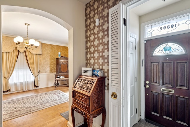 entryway with wood finished floors, wallpapered walls, arched walkways, wainscoting, and a notable chandelier