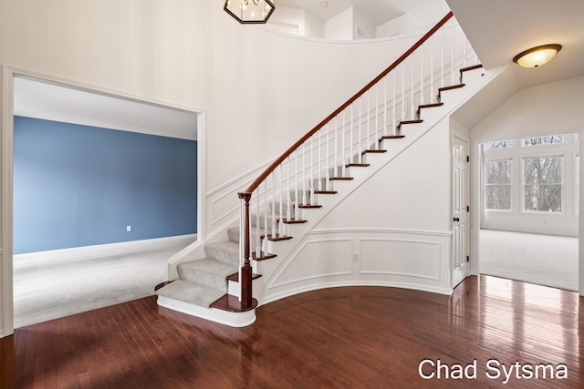 stairway with a high ceiling, a decorative wall, wood finished floors, and carpet flooring