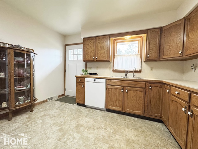 kitchen with light countertops, white dishwasher, a sink, and brown cabinets